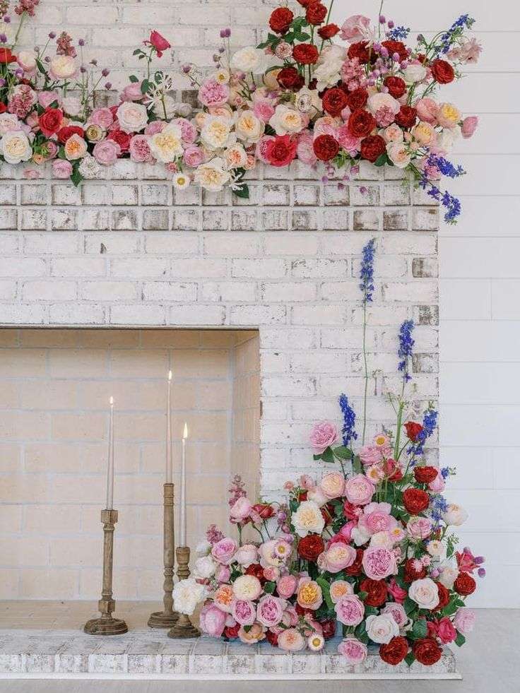 Red and pink garden roses with delphinium massed over a whitewashed fireplace
