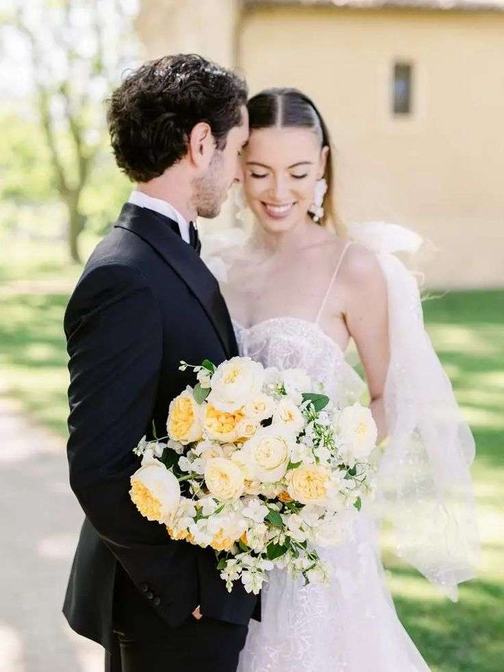 Bride and groom embracing outdoors, bride holding yellow and cream garden rose bouquet