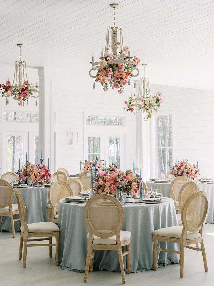 Reception room with flower-draped chandeliers over pastel-set round tables