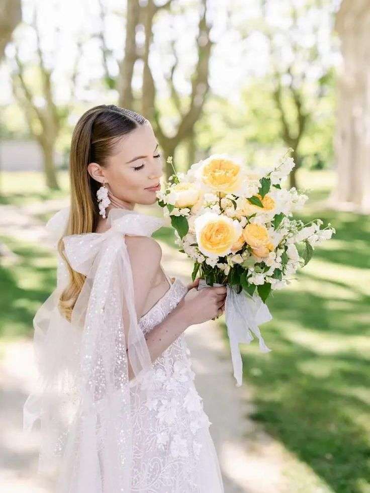 Bride smelling a yellow and white garden rose bouquet in a tree-lined park