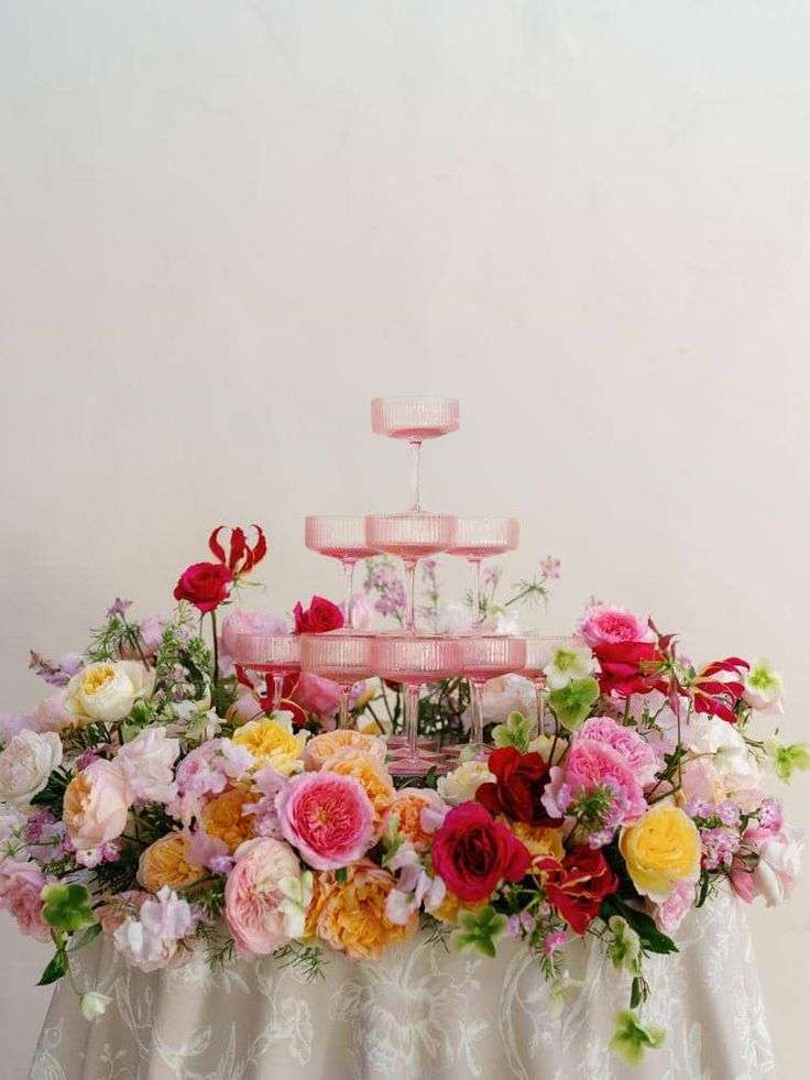Tiered pink glassware surrounded by a colorful garden rose table garland