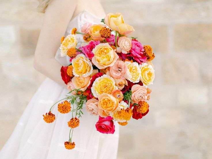 A bouquet of yellow, orange and coral garden roses held against a pale wedding gown.