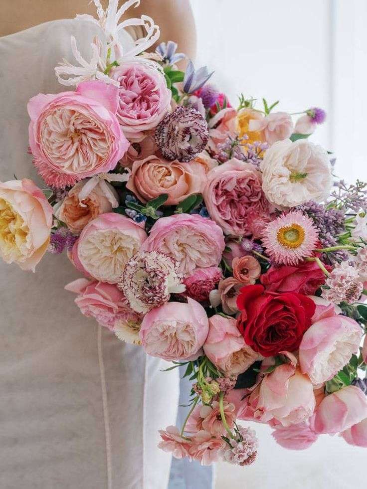 Bride holds an asymmetrical bouquet of pink and red garden roses with strawflower