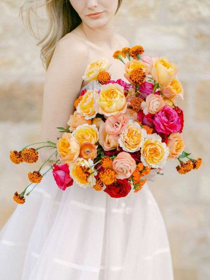 Bride holds a vibrant bouquet of yellow, orange and hot pink garden roses