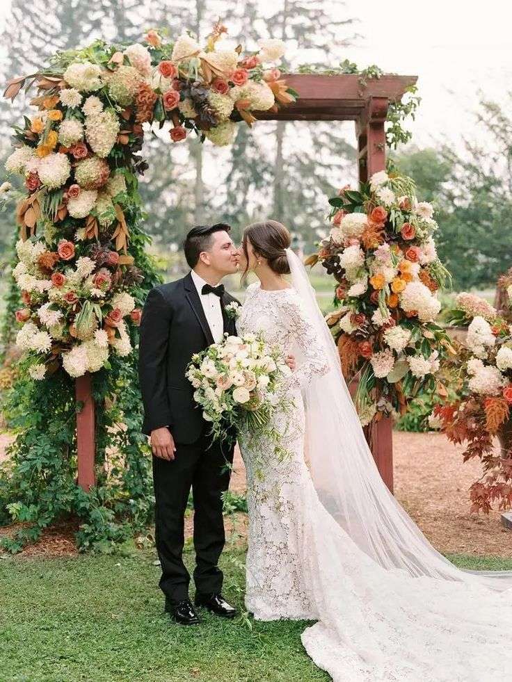 Bride and groom kiss beneath a floral arch of peach and cream blooms