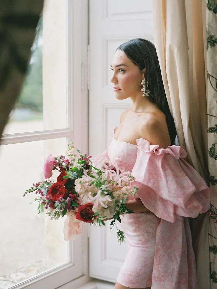 Bride in pink gown holding a David Austin garden rose bouquet by a window