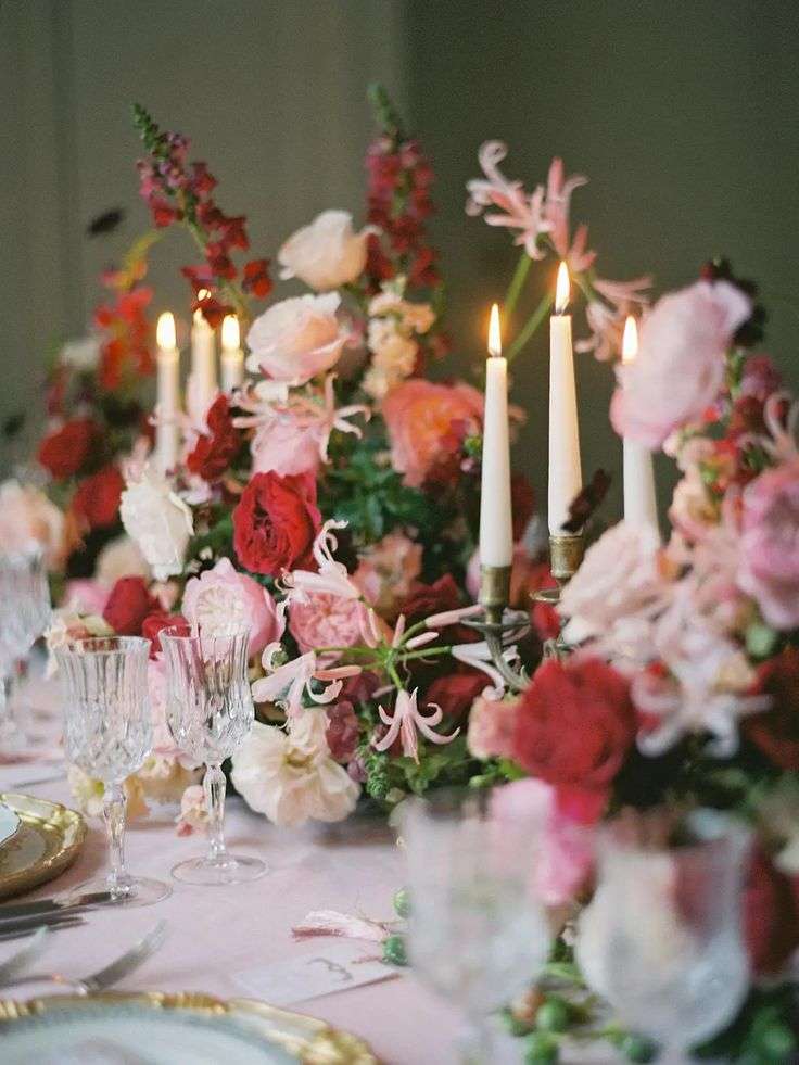 Long wedding table runner of red and pink garden roses with lit taper candles