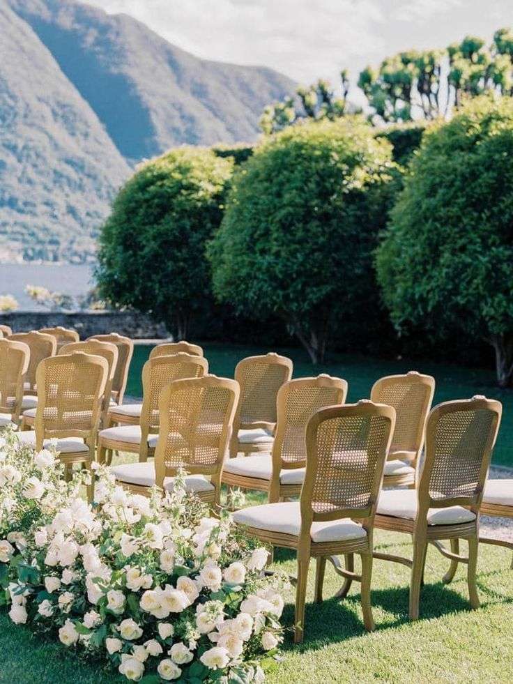Rows of cane ceremony chairs beside a white rose-lined aisle and lake view