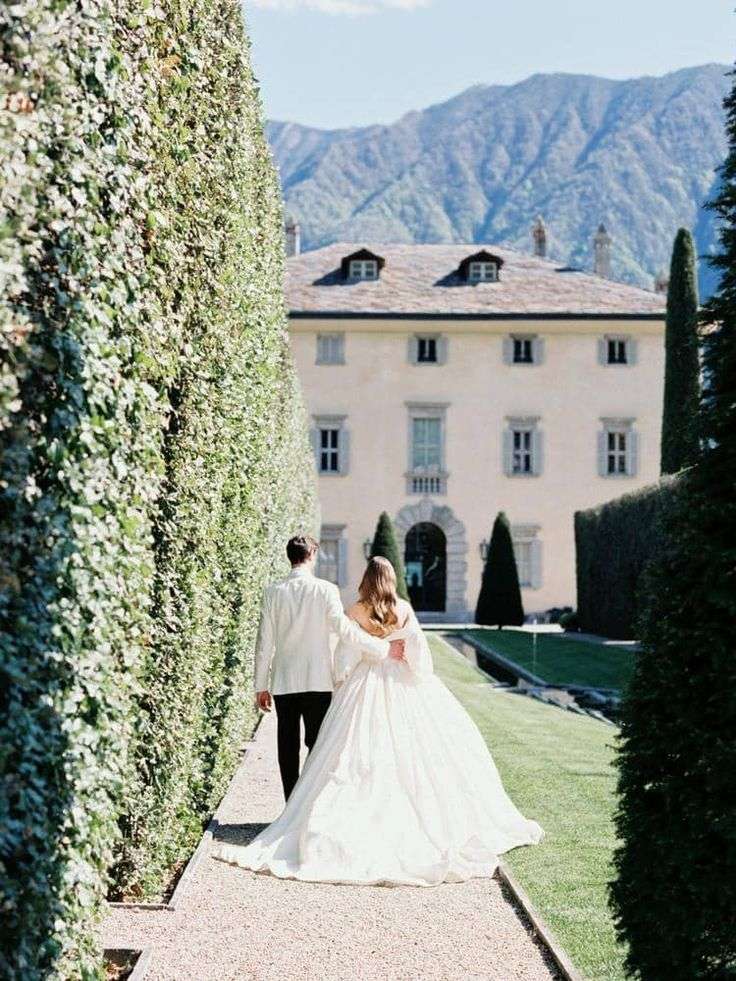 Bride and groom walking a hedge-lined path toward an Italian villa