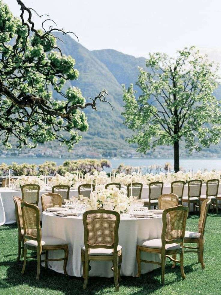 Reception table set beside a lake with mountain backdrop and white floral centerpiece