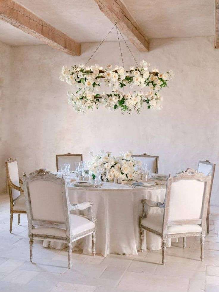 Round wedding table beneath a white garden rose hoop chandelier in a rustic room