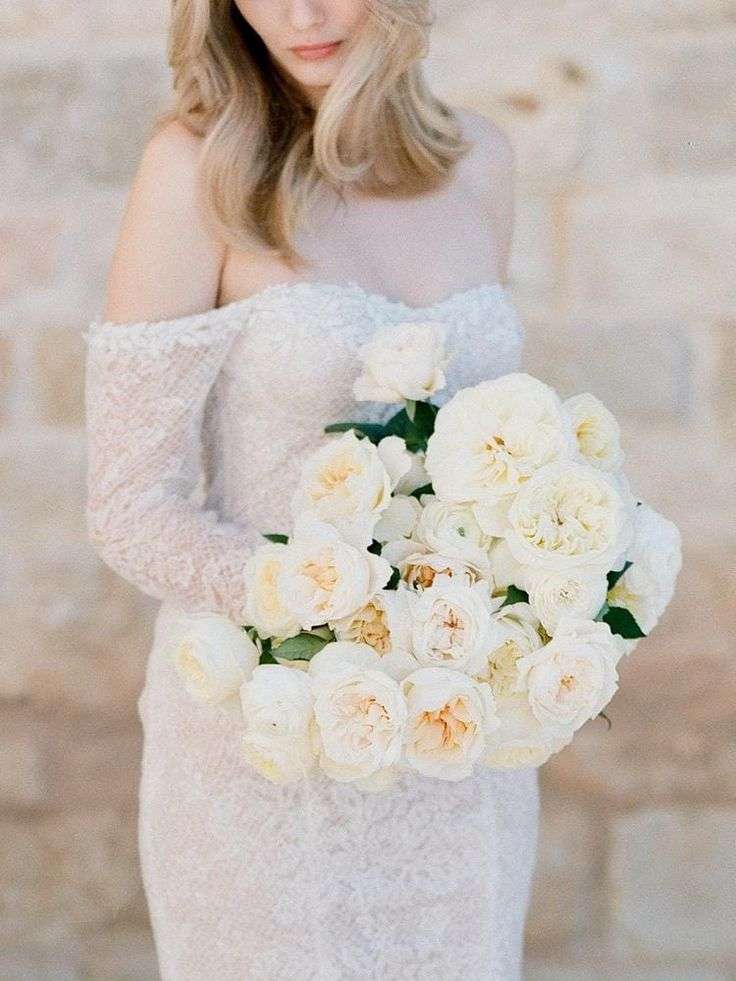 A bouquet of white and cream garden roses held against a lace wedding gown.