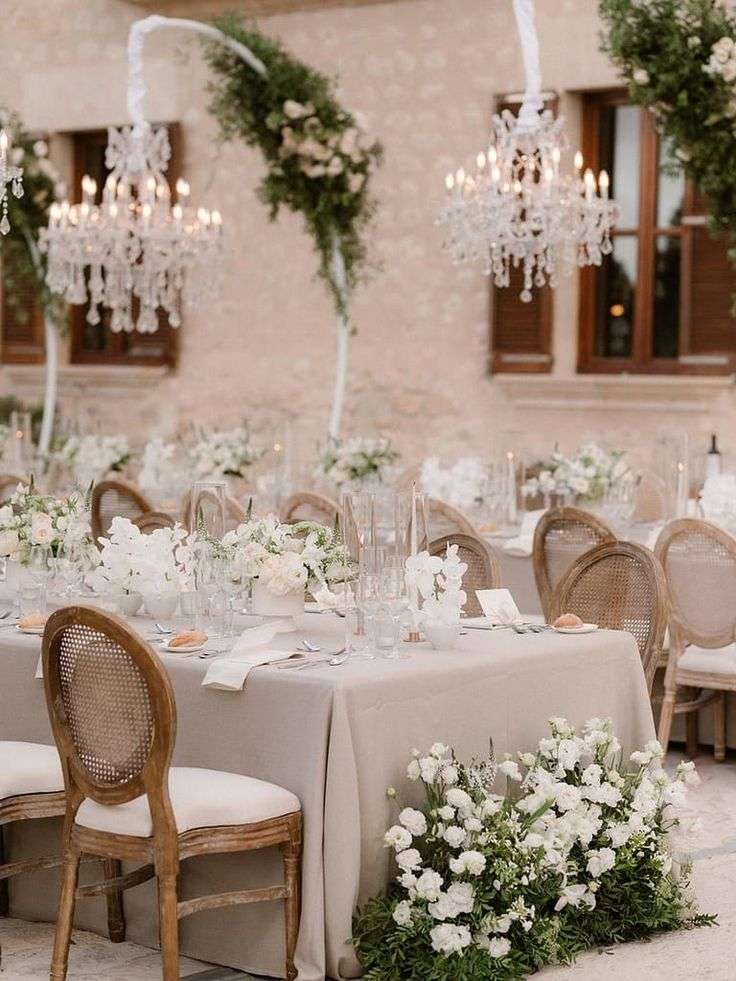 Reception table with rattan chairs and white blooms in front of the castle facade