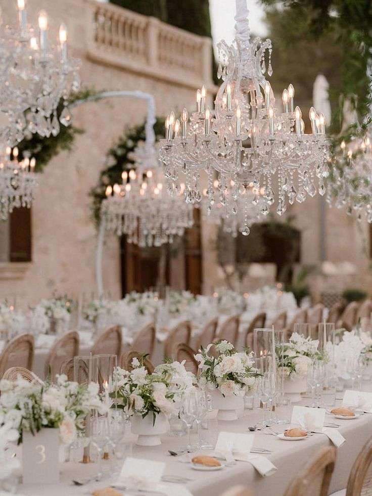 Crystal chandeliers over a long reception table with white garden rose centerpieces