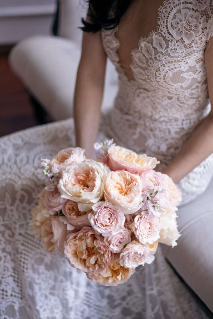 Bride seated holding a peach and pink garden rose bouquet