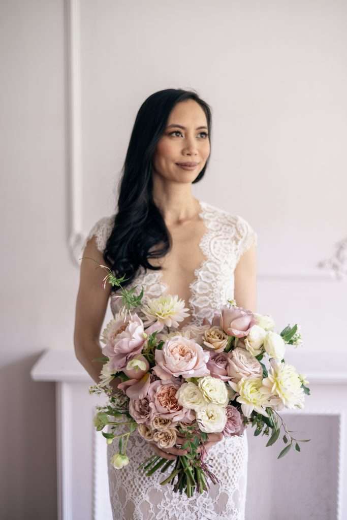 Bride by a mantel holding a blush and mauve garden rose bouquet