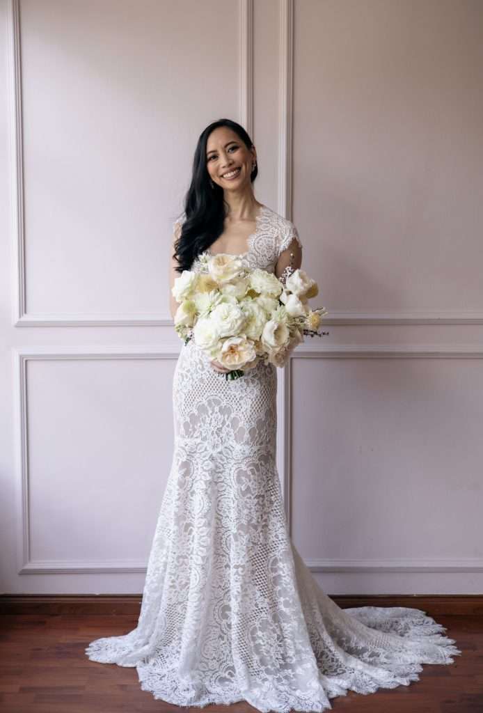 Bride in lace gown smiling with a round white bridal bouquet