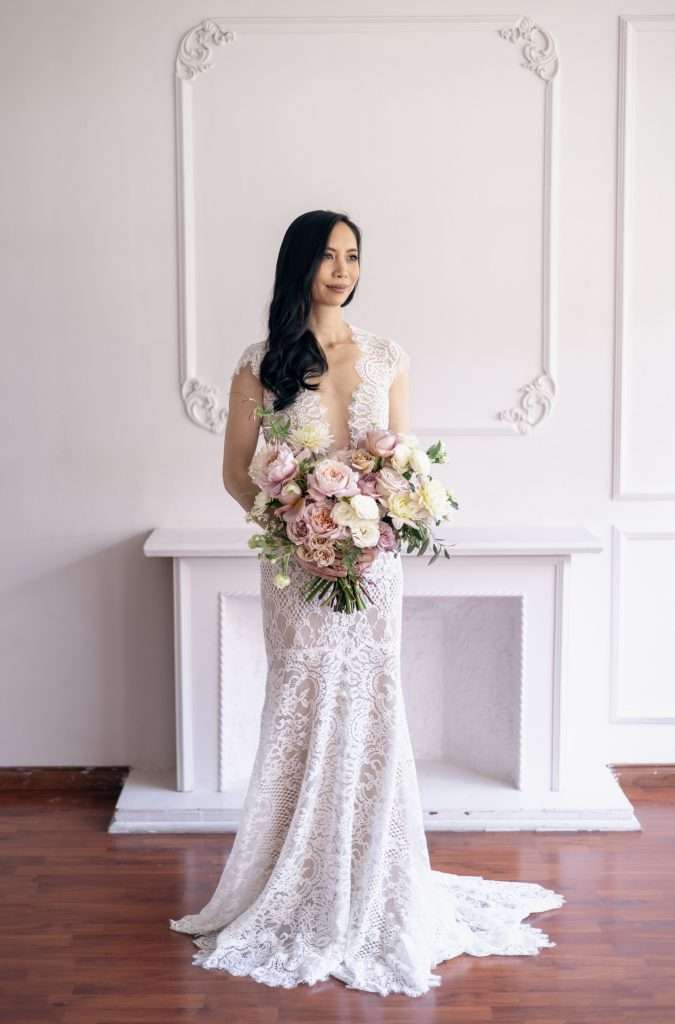 Bride standing by a mantel with a soft blush and mauve bouquet