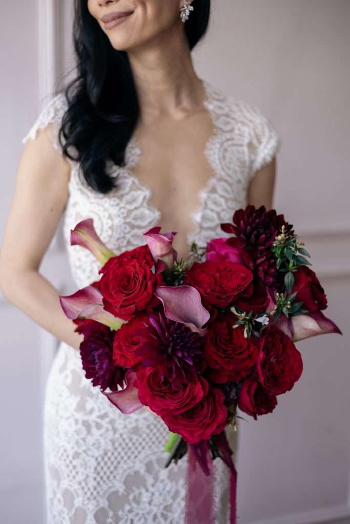 Bride holding a deep red garden rose and calla lily bouquet with pink ribbon