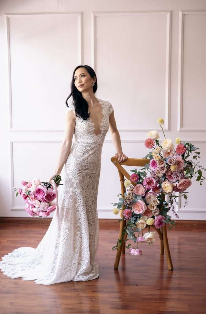 Bride with a pink bouquet standing beside a chair dressed with garden roses