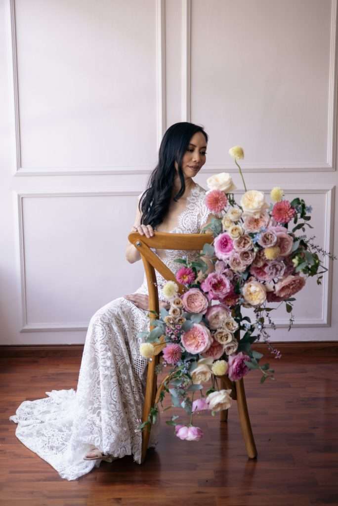 Bride seated on a chair styled with a cascading pink floral installation
