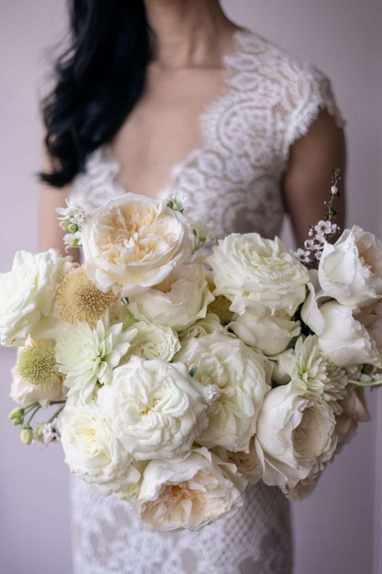A bridal bouquet of cream and white garden roses held against a lace gown.