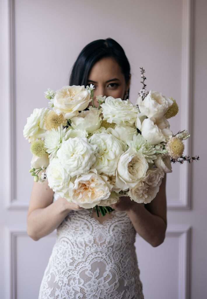 Bride holds an all-white garden rose bouquet up over her face