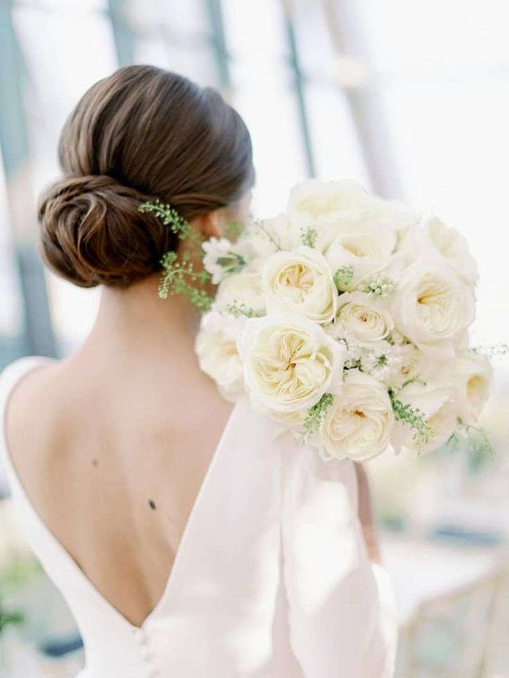 Bride from behind with low bun holding a round ivory garden rose bouquet