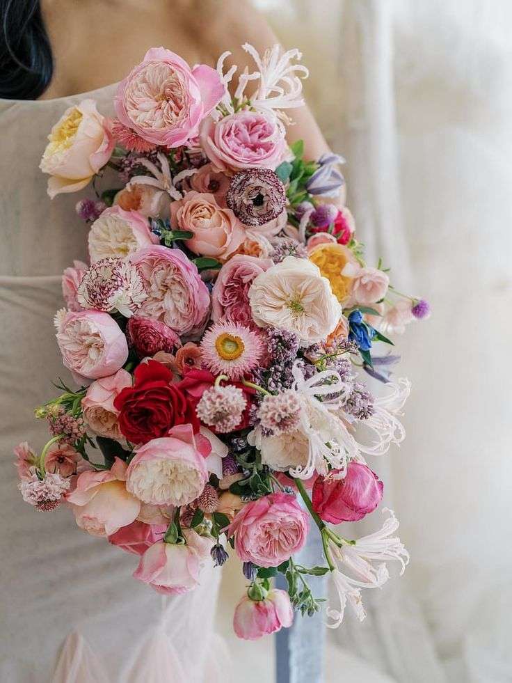 A bridal bouquet of pink, cream and coral garden roses held against a white gown.