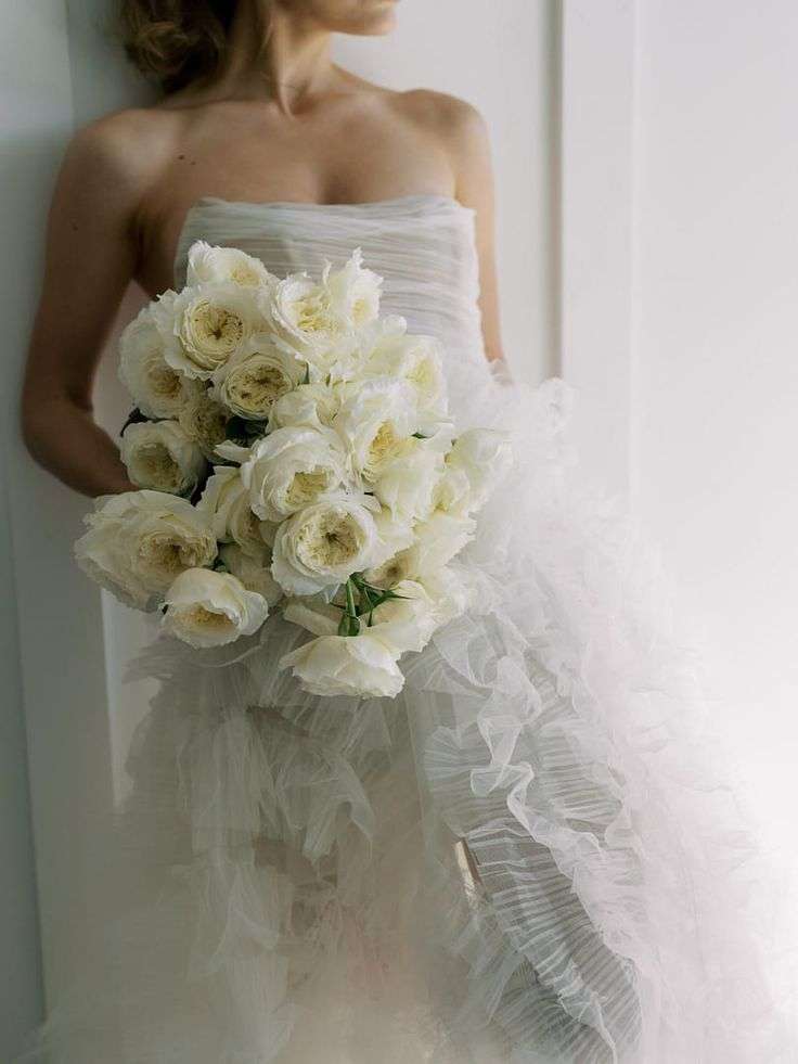 Bride in ruffled tulle gown holding a cascading white garden rose bouquet