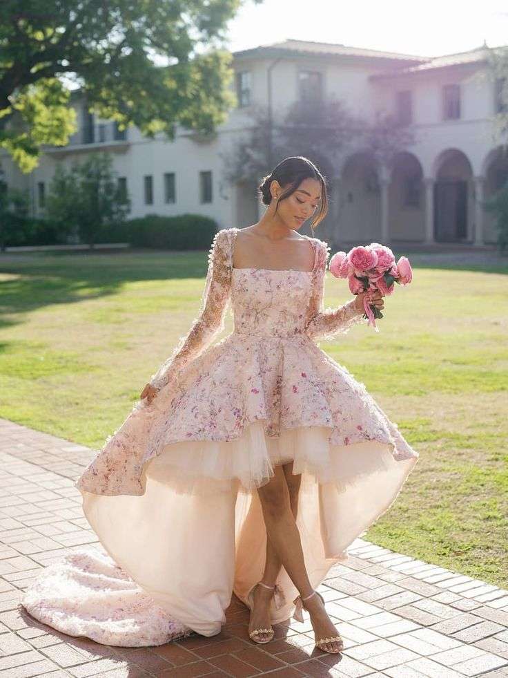 Bride in a high-low floral dress carrying pink garden roses on a garden path