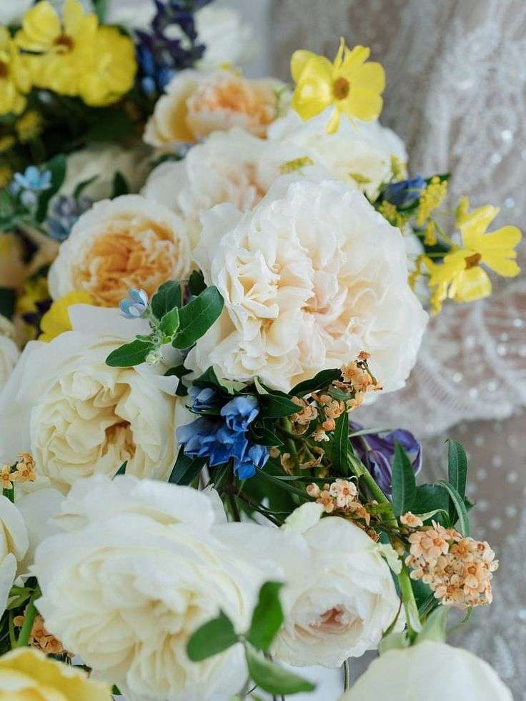 Close-up of ivory garden roses with yellow daisies and blue delphinium sprigs