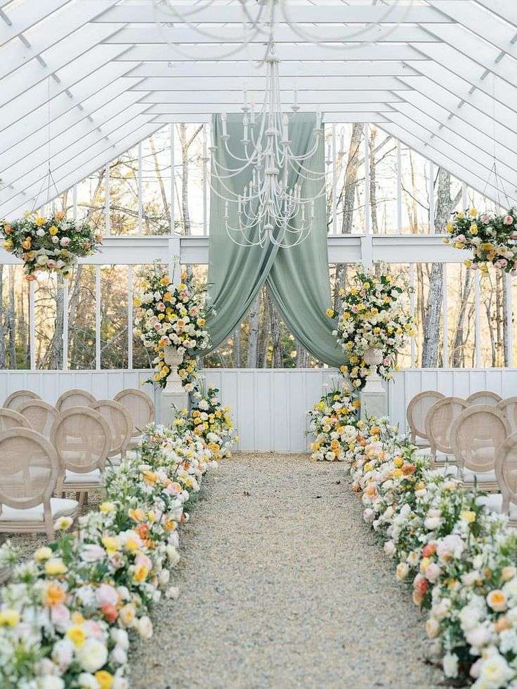 Glasshouse wedding ceremony aisle lined with yellow and white garden rose arrangements