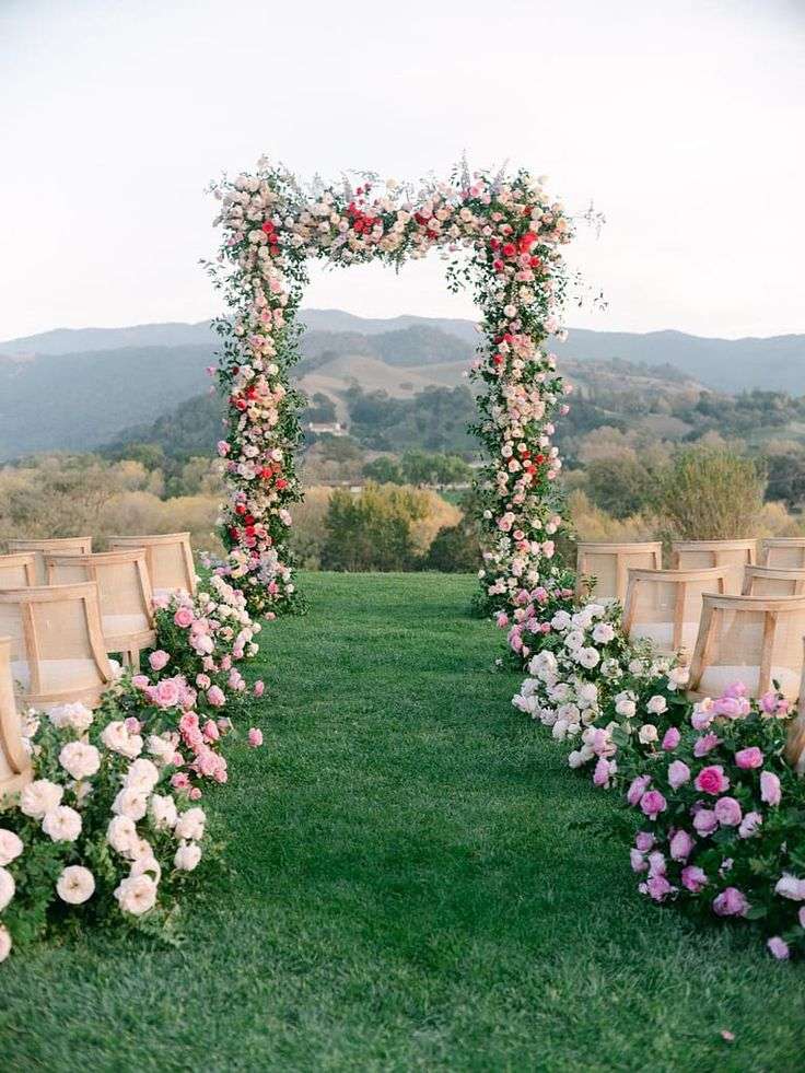 Rose-covered wedding arch framing a mountain view with petal-lined aisle