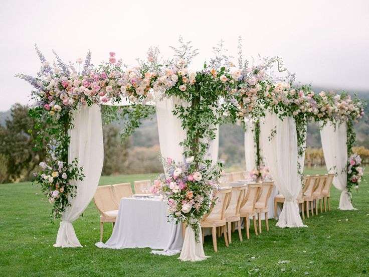 Draped wedding arbor dressed in garden roses and greenery over an outdoor reception
