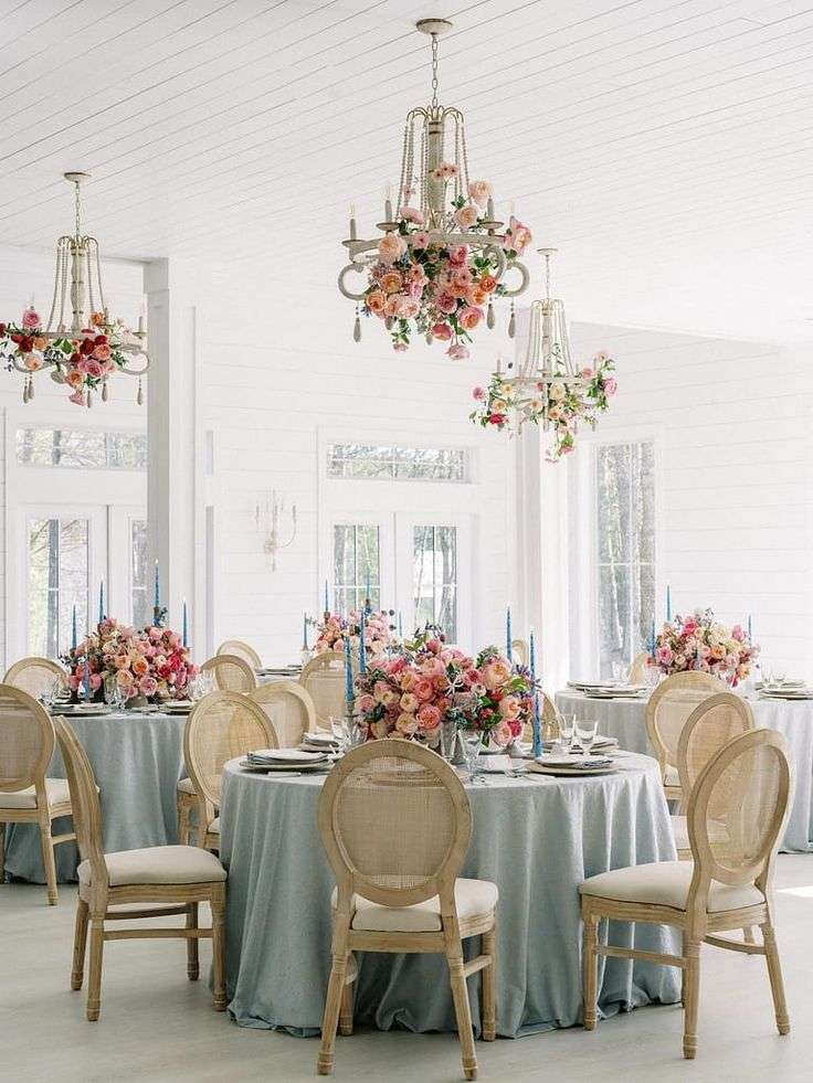 Garden rose chandeliers hang over reception tables in a white pavilion